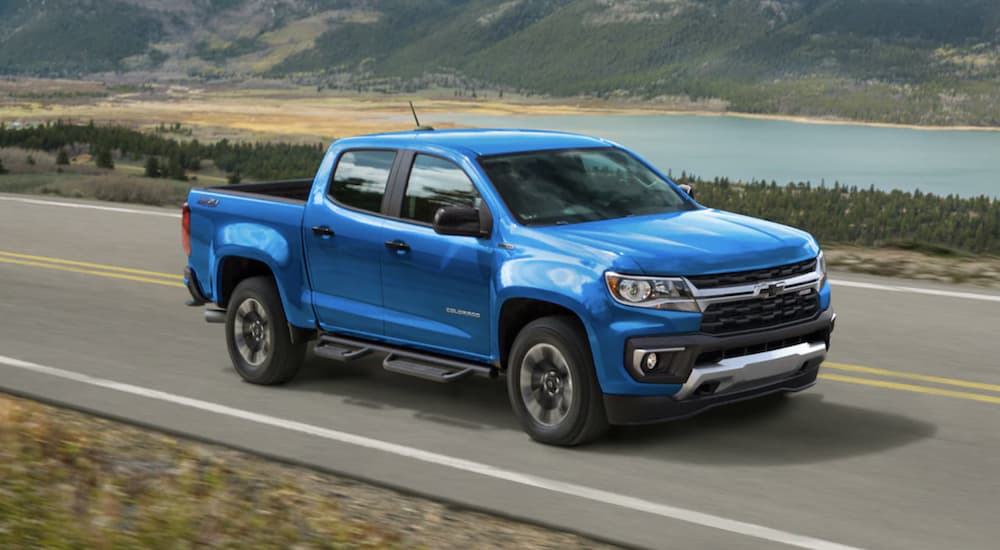 A blue 2022 Chevy Colorado Z71 is shown from the side driving on an open road past a body of water.