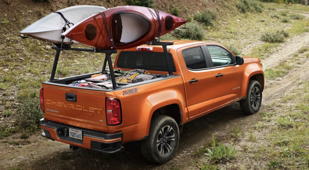 An orange 2022 Chevy Colorado is shown from the rear off-roading in a field while carrying two kayaks.