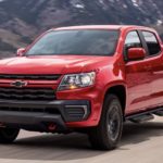 A red 2022 Chevrolet Colorado is shown from the side driving on an open road past a body of water.