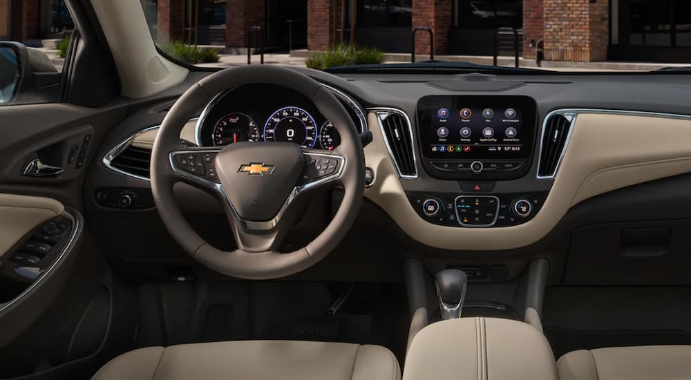 The tan and black interior of a 2022 Chevy Malibu shows the steering wheel and infotainment screen.