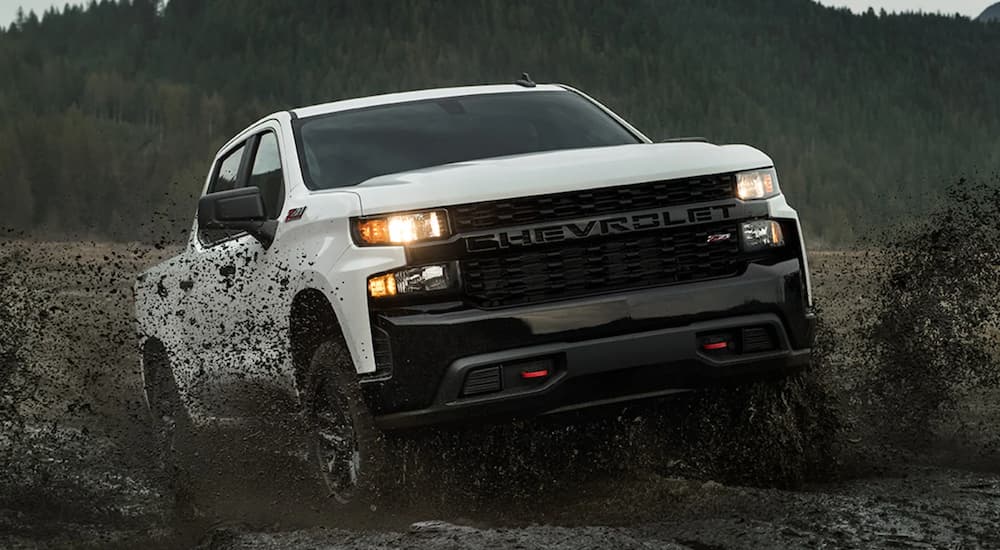 A white 2022 Chevy Silverado 1500 Z71 is shown from the front off-roading in a muddy field.