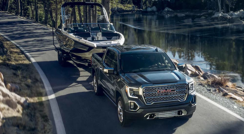 A black 2022 GMC Sierra 1500 is shown towing a boat on an open road past a stream.