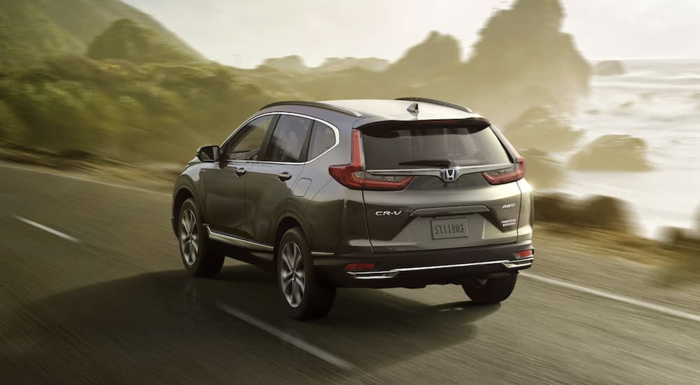 A grey 2022 Honda CR-V Hybrid Touring is shown from the rear driving on an open road past a body of water.