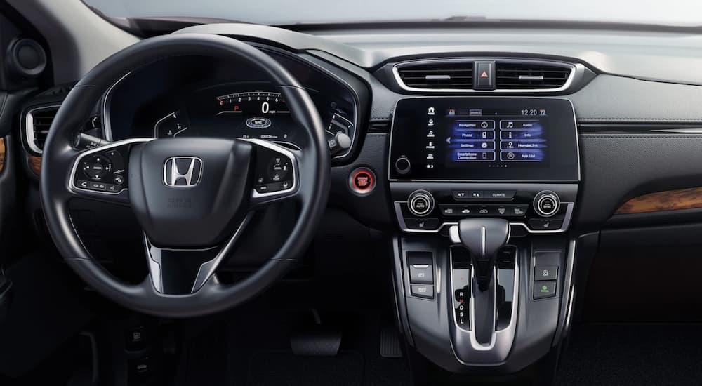The black interior of a 2022 Honda CR-V Hybrid Touring shows the steering wheel and infotainment screen.