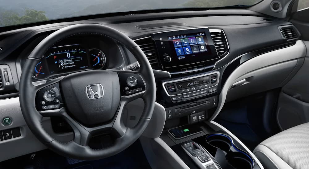 The black interior of a 2022 Honda Pilot Elite shows the steering wheel and infotainment screen.