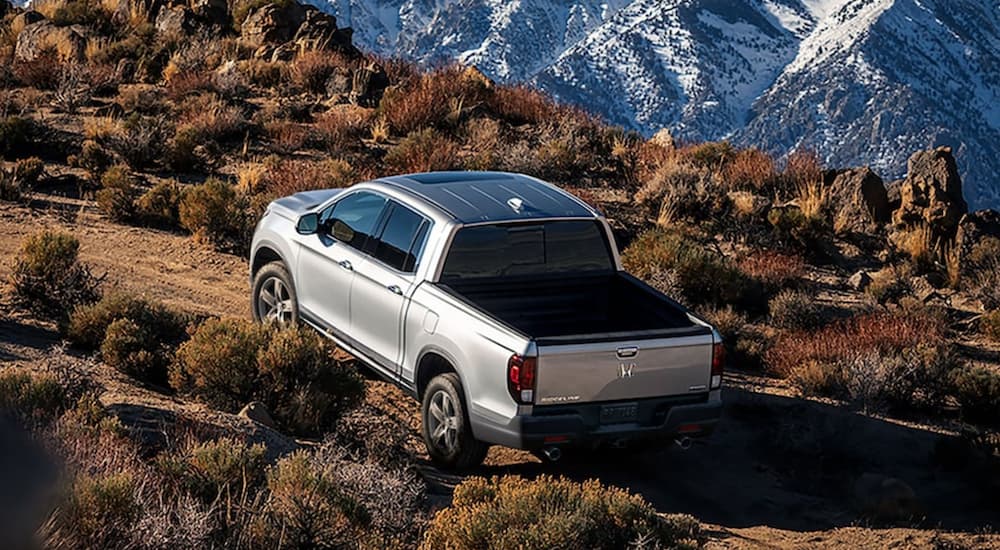 A silver 2022 Honda Ridgeline RTL-E is shown from the rear off-roading in the mountains.