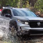 A silver 2022 Honda Ridgeline Sport is shown from the front off-roading through a river.