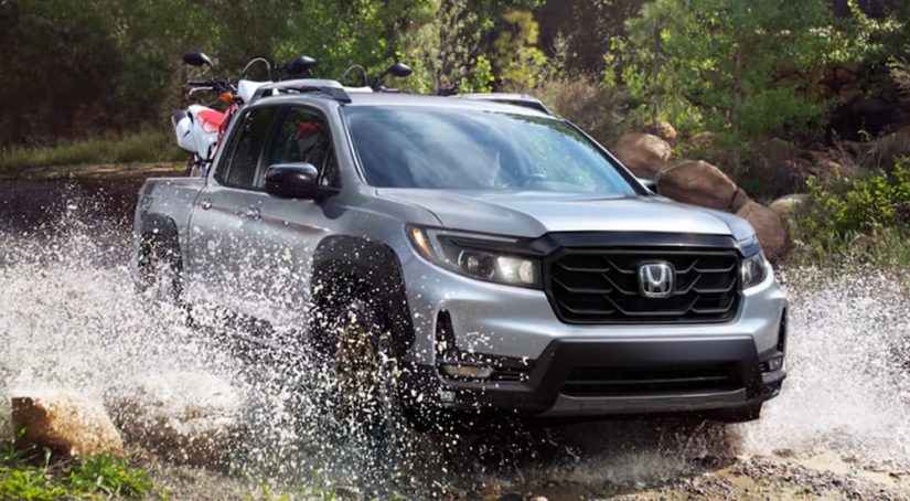 A silver 2022 Honda Ridgeline Sport is shown from the front off-roading through a river.