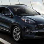 A blue 2022 Kia Sportage is shown from the front driving over a bridge.