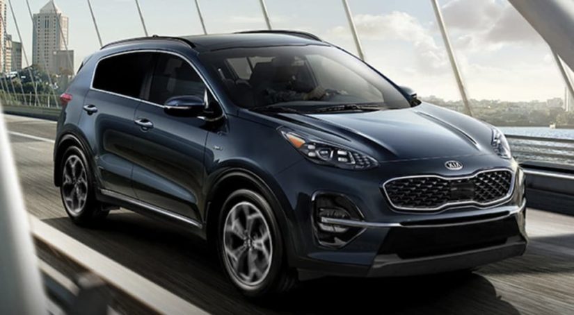 A blue 2022 Kia Sportage is shown from the front driving over a bridge.