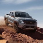 A grey 2022 Nissan Frontier is shown from the front off-roading in the mountains.