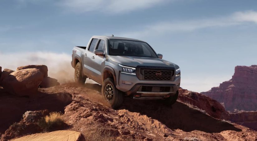 A grey 2022 Nissan Frontier is shown from the front off-roading in the mountains.