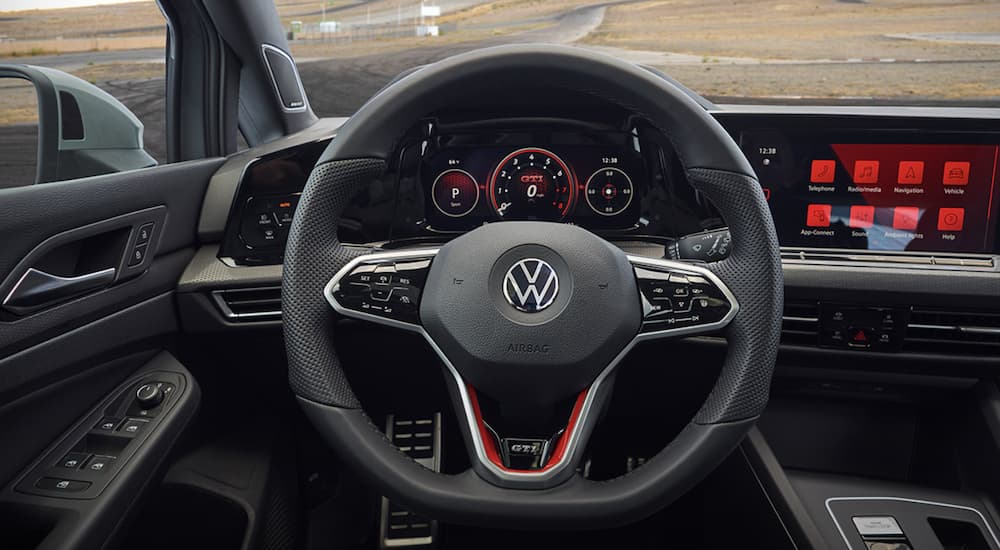 The black interior of a 2022 Volkswagen Golf GTI shows the steering wheel and infotainment screen.