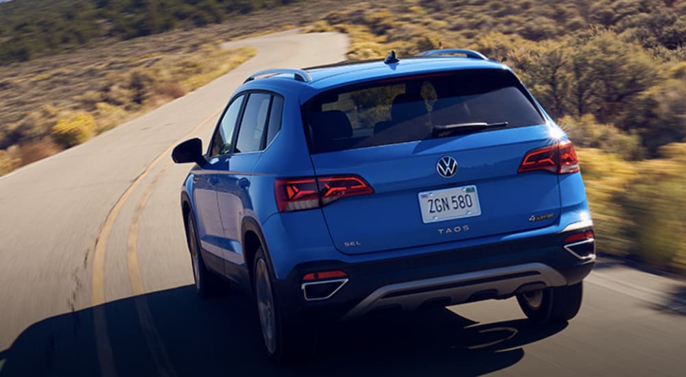 A blue 2022 Volkswagen Taos is shown from the rear driving on an open road.