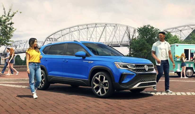 A blue 2022 Volkswagen Taos is shown from the side parked in front of a bridge after winning a 2022 Volkswagen Taos vs 2022 Jeep Compass comparison.