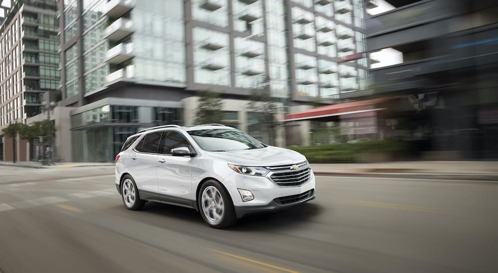 A white 2018 Chevy Equinox is shown from the side driving through a city.
