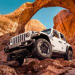 A white 2020 Jeep Wrangler is shown off-roading on red rocks.