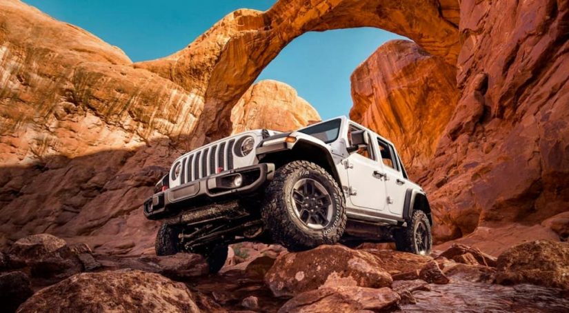 A white 2020 Jeep Wrangler is shown off-roading on red rocks.