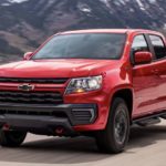 A red 2021 Chevy Colorado Trail Boss is shown from the front driving on an open road after leaving a Chevy truck dealer.