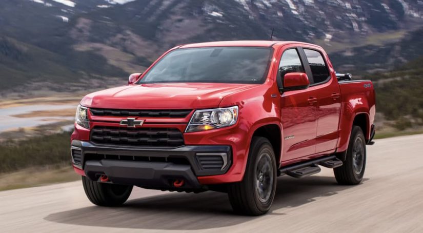 A red 2021 Chevy Colorado Trail Boss is shown from the front driving on an open road after leaving a Chevy truck dealer.