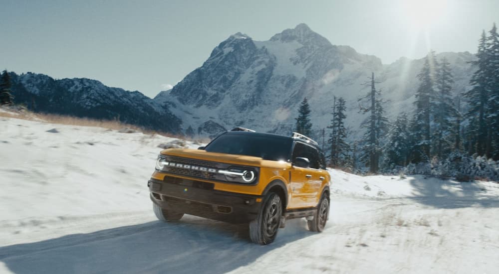 A gold 2021 Ford Bronco Sport is shown driving on a snow-covered road.