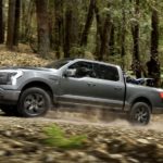 A grey 2022 Ford F-150 Lightning is shown from the side driving through the woods after leaving a Ford F-150 dealer.
