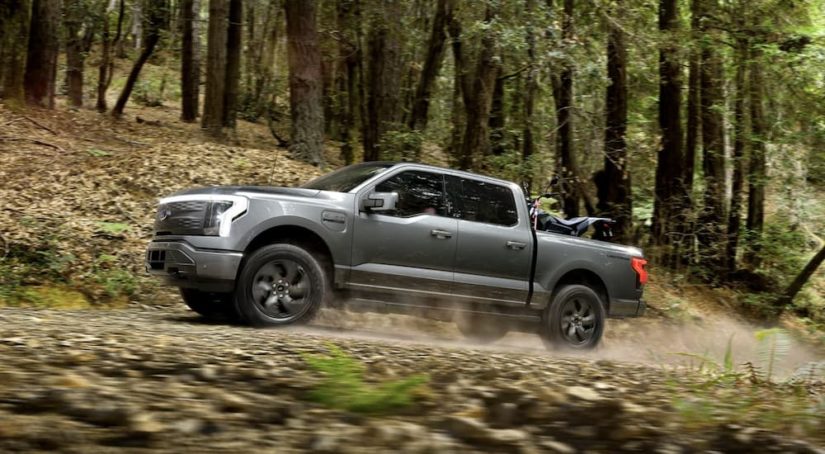 A grey 2022 Ford F-150 Lightning is shown from the side driving through the woods after leaving a Ford F-150 dealer.