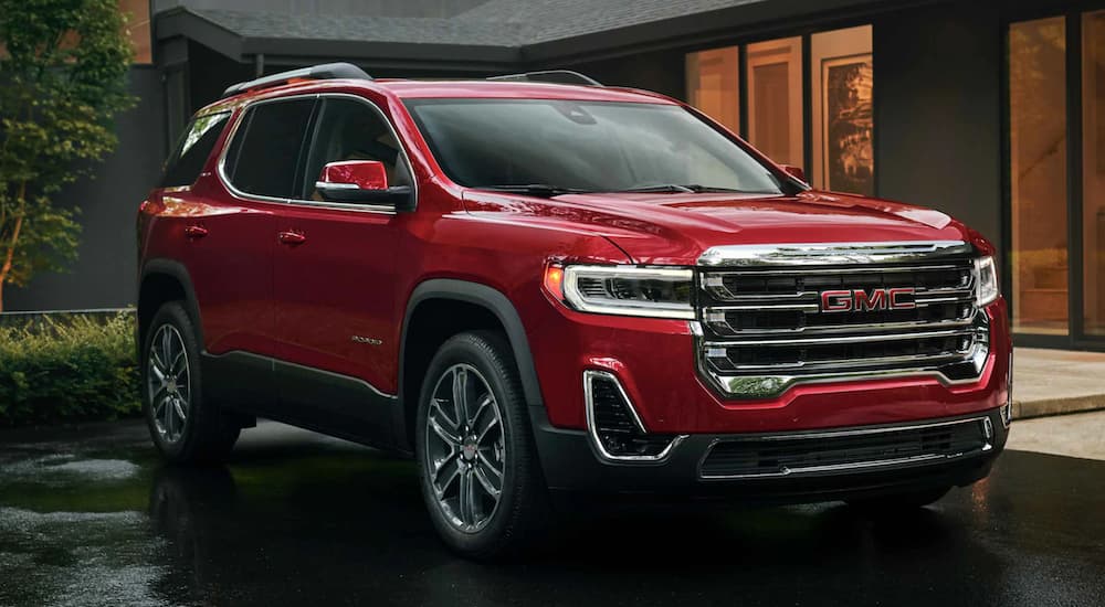 A red 2022 GMC Acadia is shown from the side parked in front of a modern house.