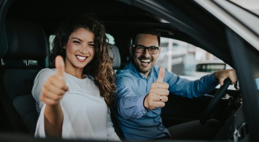 A couple is shown giving a thumbs up inside of a car after they leaned how to sell your car.