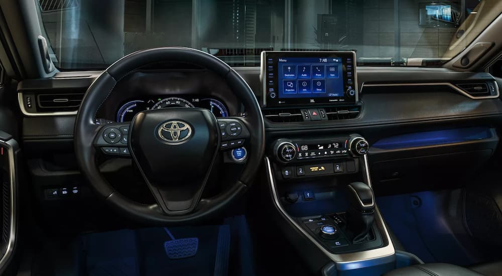 The black interior of a 2022 Toyota RAV4 Hybrid XSE shows the steering wheel and infotainment screen.