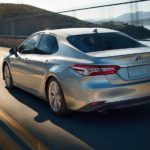 A silver 2020 Toyota Camry XLE Hybrid is shown from the rear driving over a bridge.