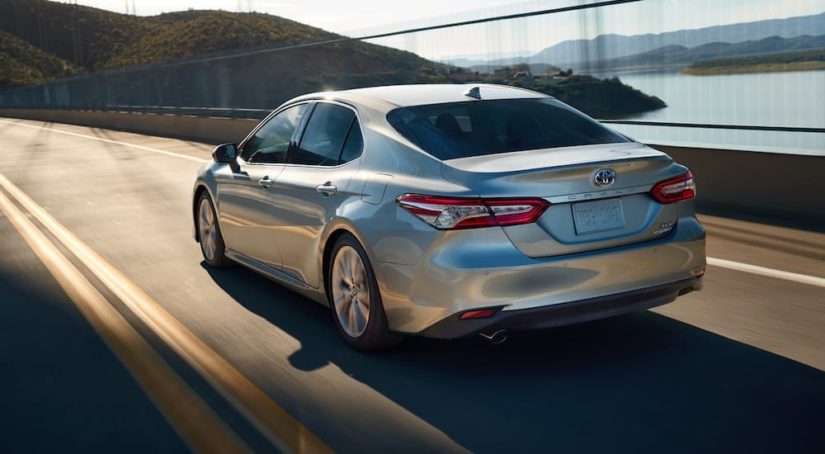 A silver 2020 Toyota Camry XLE Hybrid is shown from the rear driving over a bridge.
