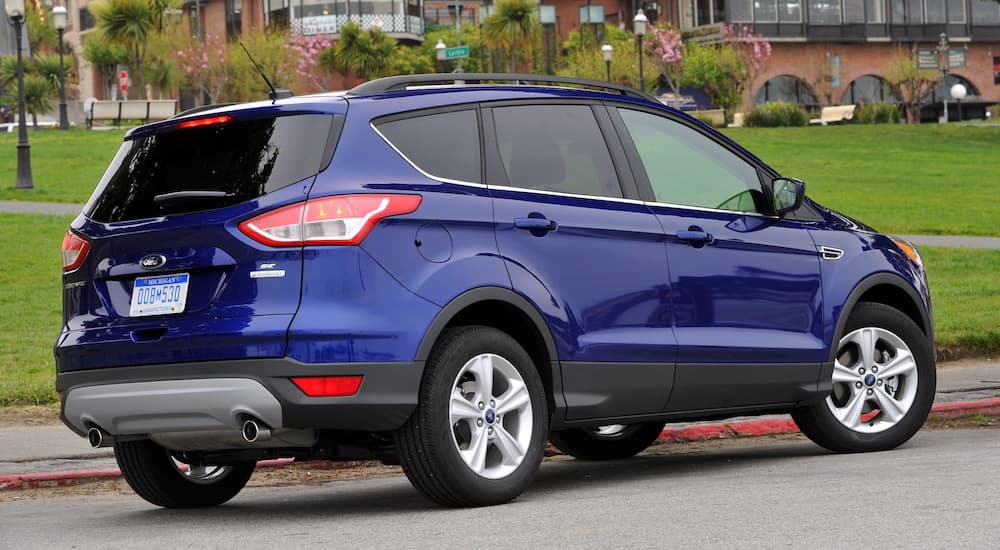 A blue 2013 Ford Escape is shown from the size parked in front of a grass field.