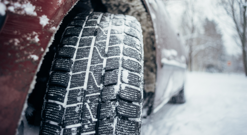 A red sedan with an all-season tire is shown in the snow.