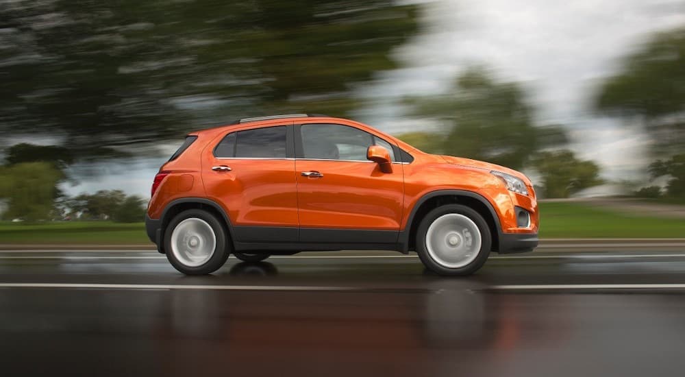 An orange 2015 Chevy Trax is shown from the side driving on an open road after leaving a used Chevrolet dealer.