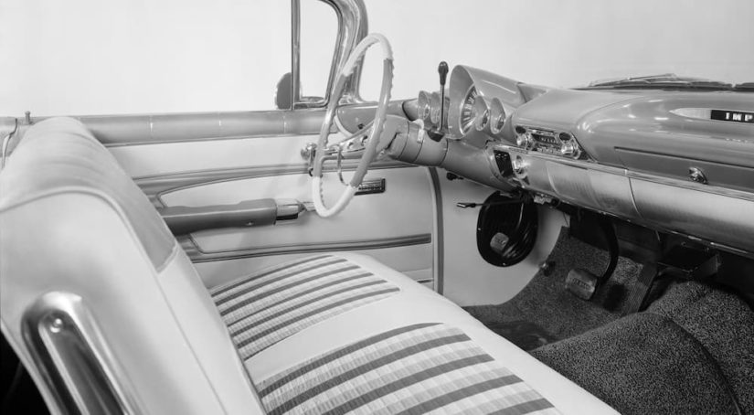 The black and white interior of a 1959 Chevy Impala shows the front seat and steering wheel.