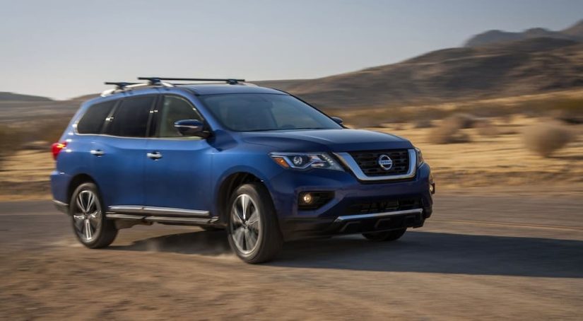 A blue 2017 Nissan Pathfinder is shown from the side off-roading in a desert after leaving a used Nissan dealership.