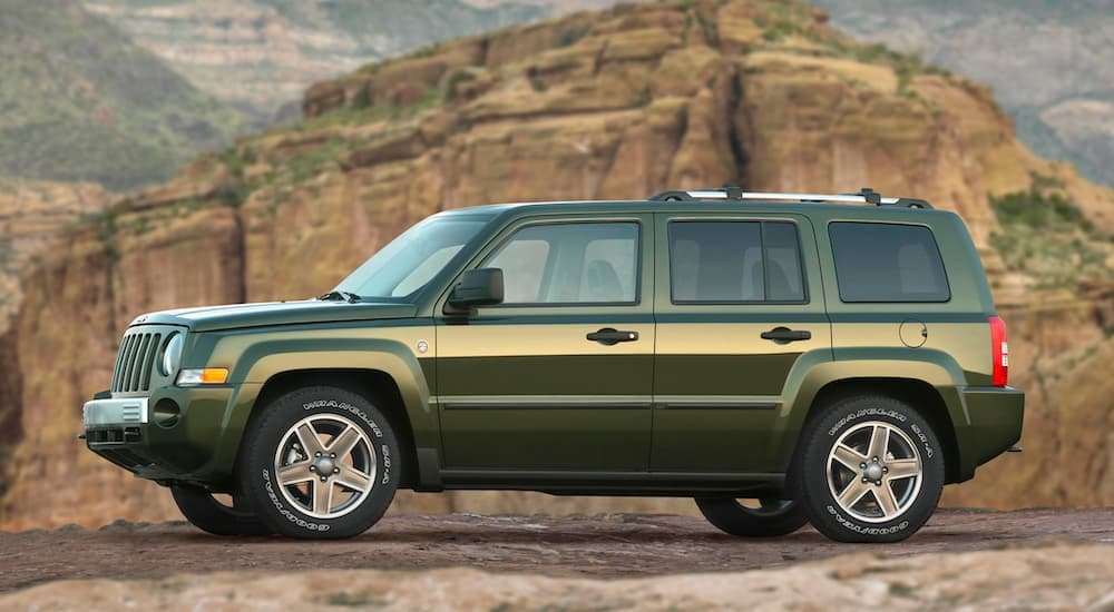 A green 2007 Jeep Patriot is shown from the side parked in the mountains.