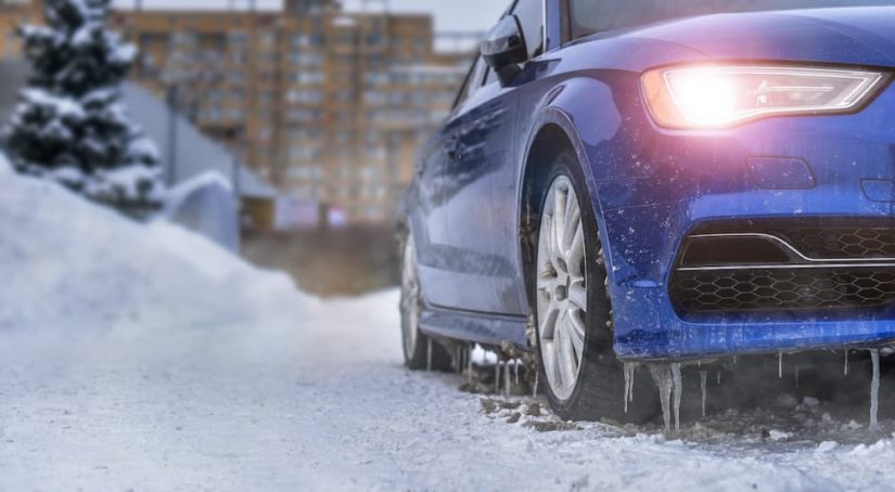 A blue car is shown idling in a snowy driveway after visiting a winter tire dealer.