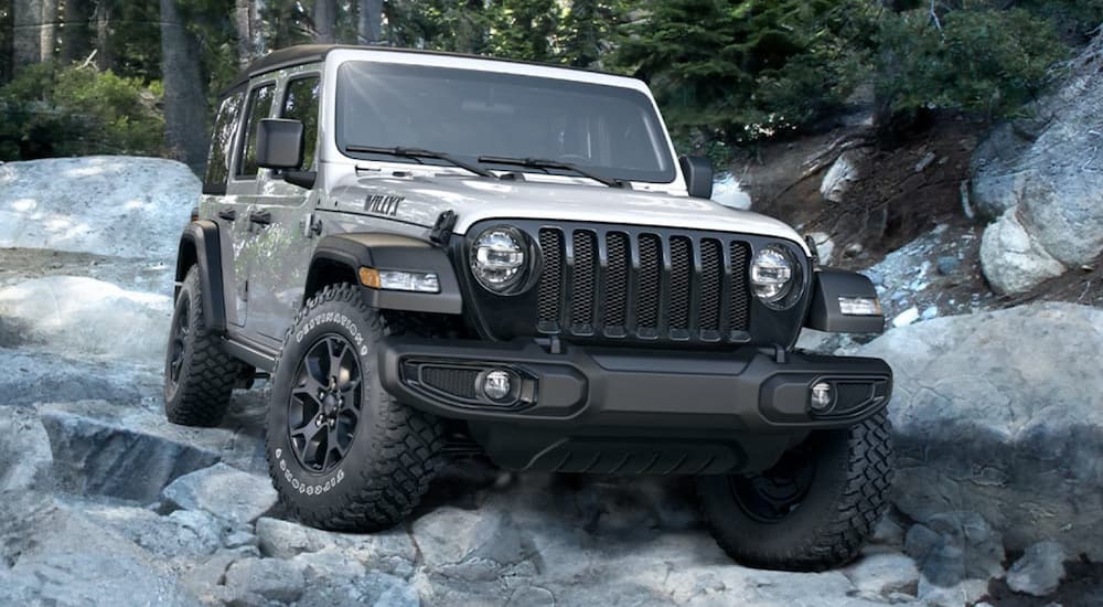 A silver 2020 Jeep Wrangler Willys Edition is shown off-roading on grey rocks.