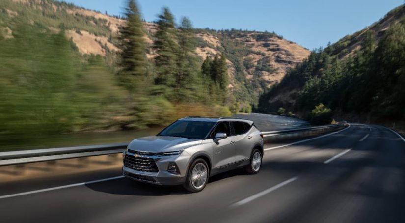 A silver 2022 Chevy Blazer Premier is shown driving on a highway through the mountains.