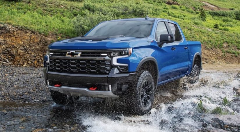 A blue 2022 Chevy Silverado 1500 ZR2 is shown off-roading through a puddle.