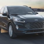 A black 2022 Ford Escape Elite is shown driving on a coastal road past the ocean.