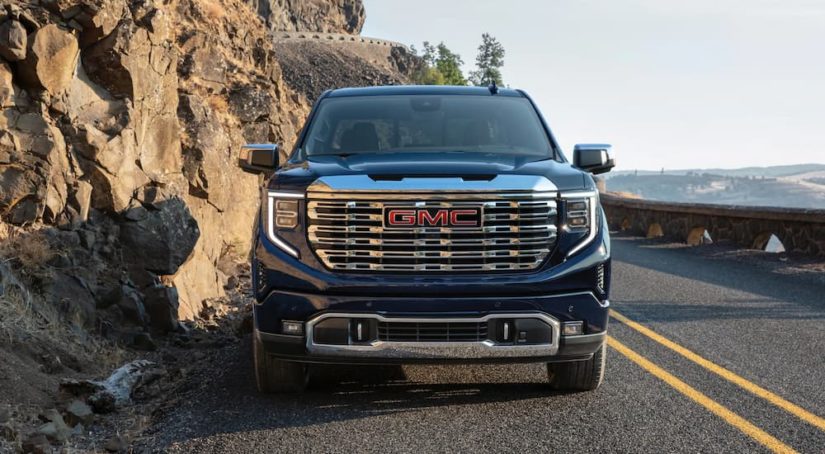 A blue 2022 GMC Sierra 1500 Denali Ultimate is shown from the front parked next to a rock face.