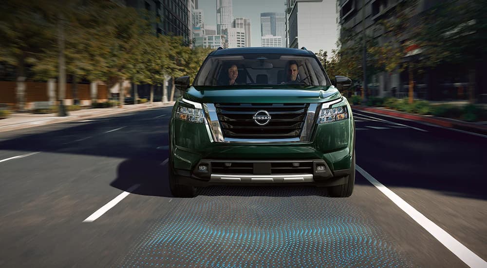 A green 2022 Nissan Pathfinder is shown on a city street with simulated intelligent forward collision warning lines.