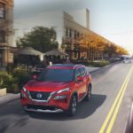 A red 2022 Nissan Rogue is shown driving down a city street.