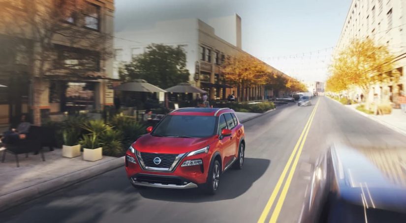 A red 2022 Nissan Rogue is shown driving down a city street.