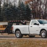 A white 2022 Ram 3500 is shown towing heavy machinery and wood beams.