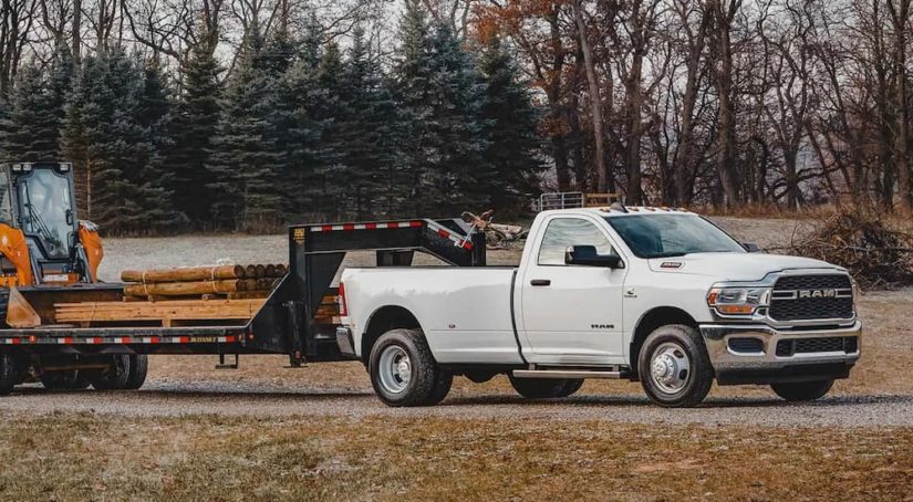 A white 2022 Ram 3500 is shown towing heavy machinery and wood beams.