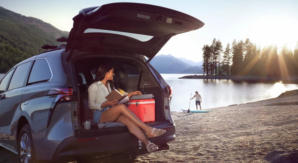 A woman is shown sitting in the rear cargo space of a 2022 Toyota Sienna near a lake.
